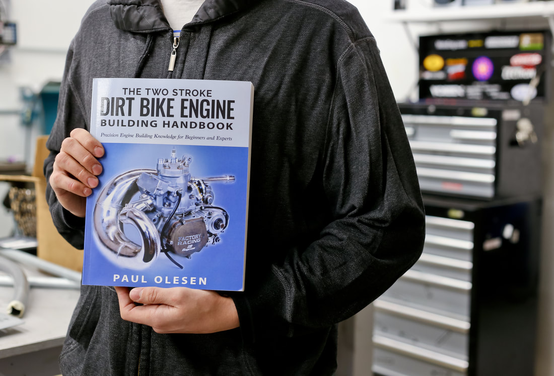 Author, Paul Olesen, holding The Two Stroke Dirt Bike Engine Building Handbook in his workshop